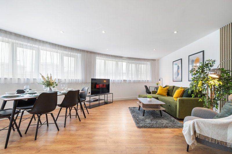 Open-plan living room with dining area, wooden floors, olive sofa and modern furnishings