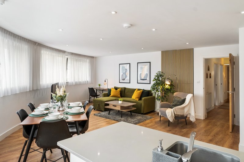 Open-plan living area with dining table, sofa, armchair, wooden flooring and large windows