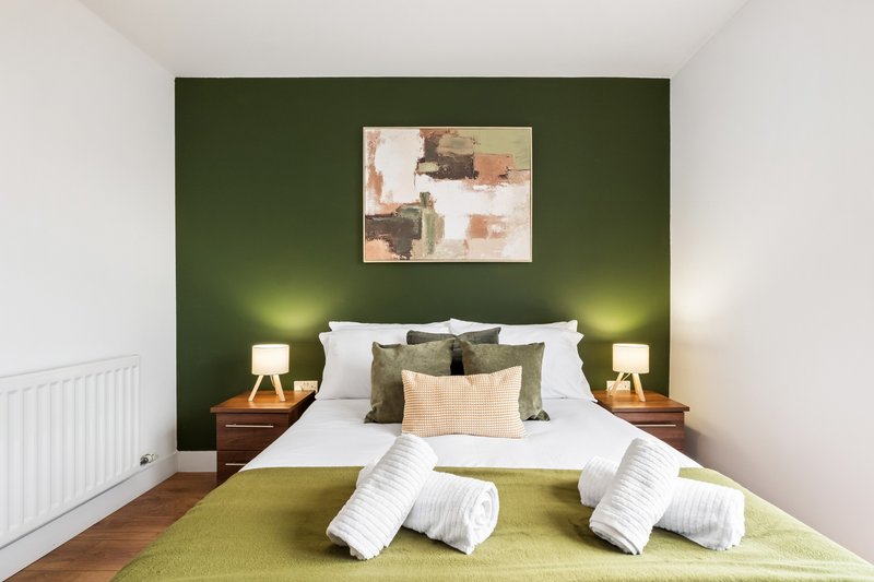 Bedroom with green accent wall, double bed, white bedding, wooden nightstands and wall art