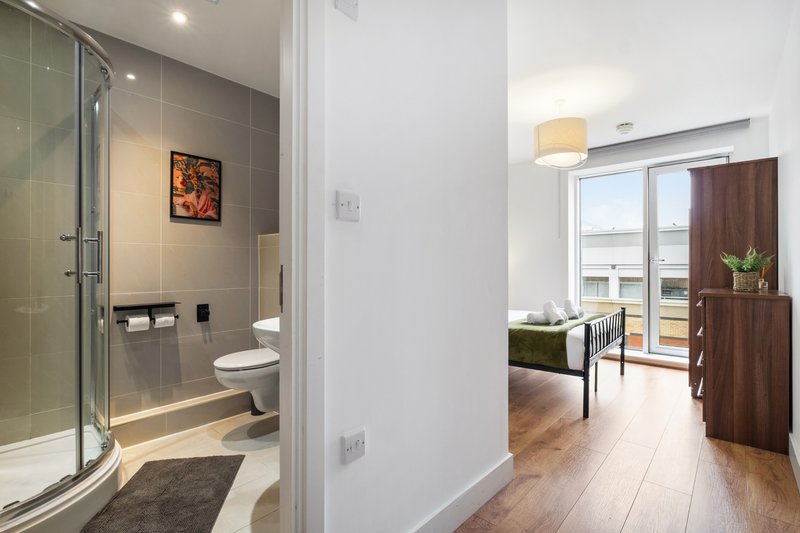 Modern bathroom with walk-in shower, toilet, and basin, adjoining hallway and bedroom area