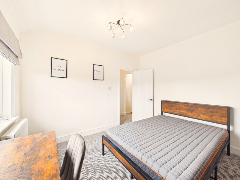 Bright bedroom with wooden bed frame, grey mattress, desk, and minimalist wall art