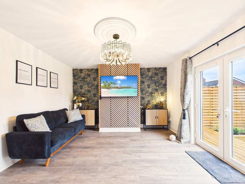 Modern living room with blue sofa, wooden flooring, decorative wall panels and glass doors to garden