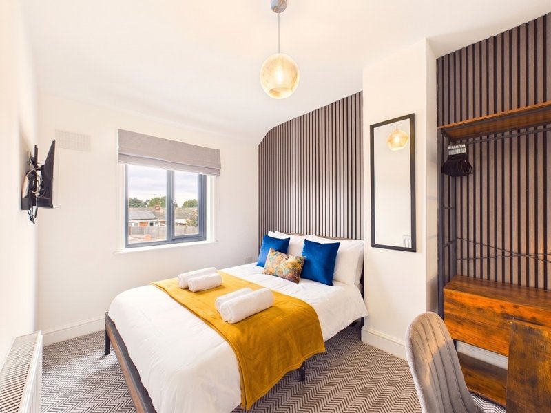 Modern bedroom with double bed, yellow throw, blue cushions, pendant light and wooden wardrobe