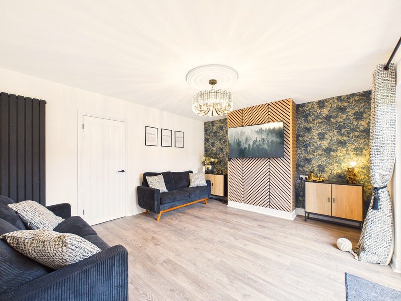 Modern living room with blue sofas, wooden flooring, patterned wallpaper and ceiling light fixture