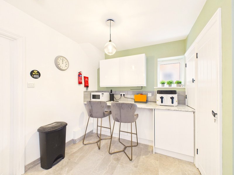 Modern kitchen with white cabinets, gray countertop, bar seating, and green accent wall
