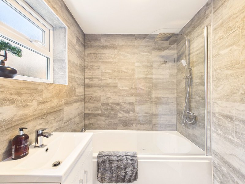 Modern bathroom with light wood tile walls, white basin, bathtub and glass shower enclosure