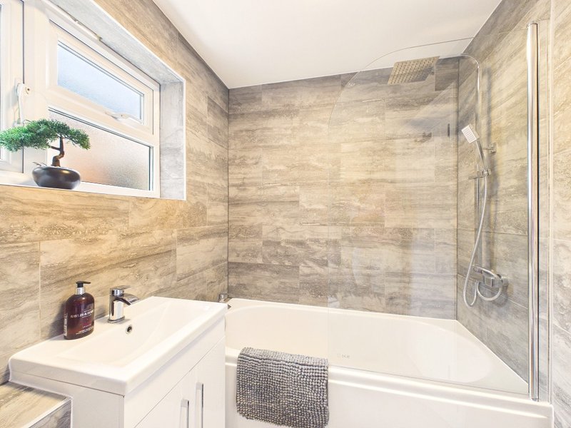 Modern bathroom with white bathtub, glass shower enclosure, stone tile walls and window