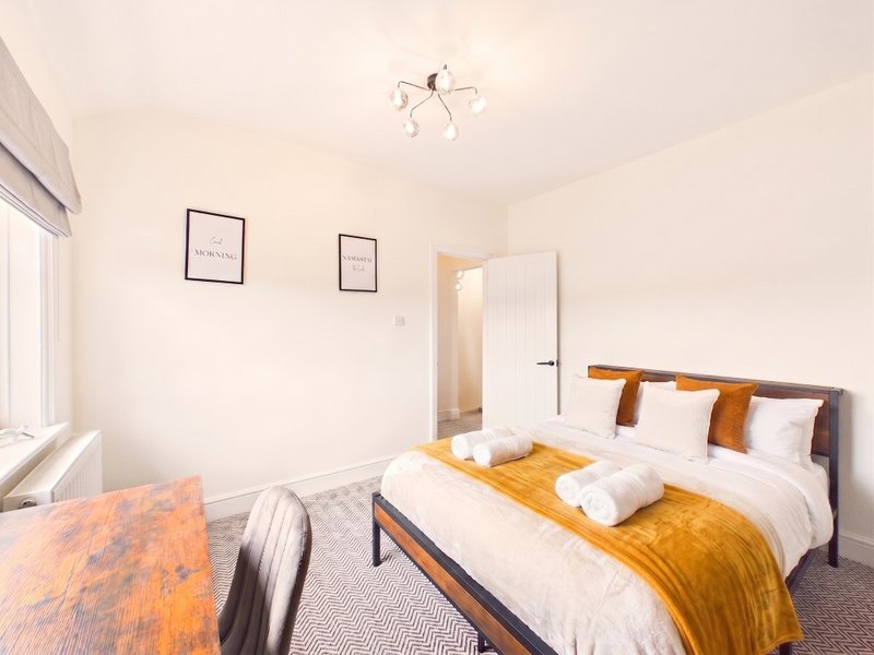 Bright bedroom with double bed, wooden desk, gold bedding, and framed wall art