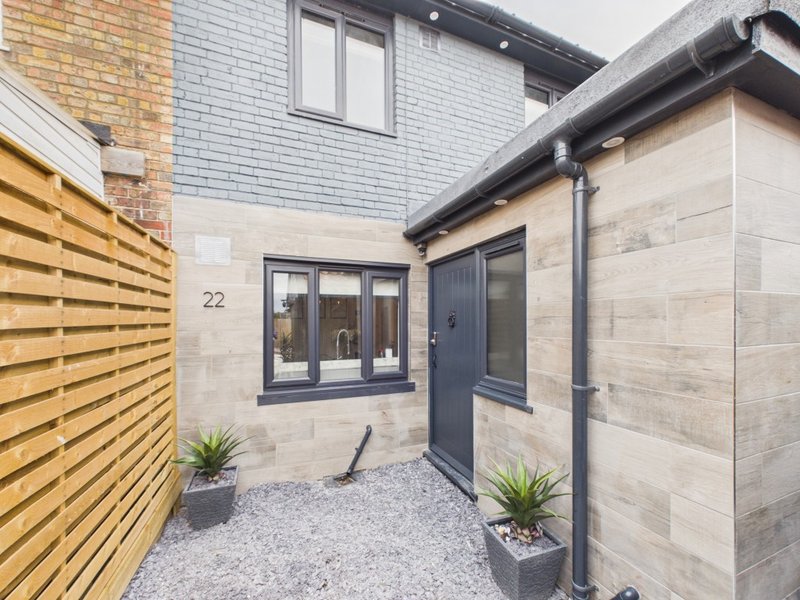 Modern courtyard entrance with wooden fencing, stone cladding, potted plants and house number 22