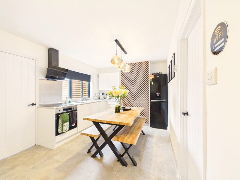 Modern kitchen with white cabinetry, wooden dining table, black appliances and pendant lighting