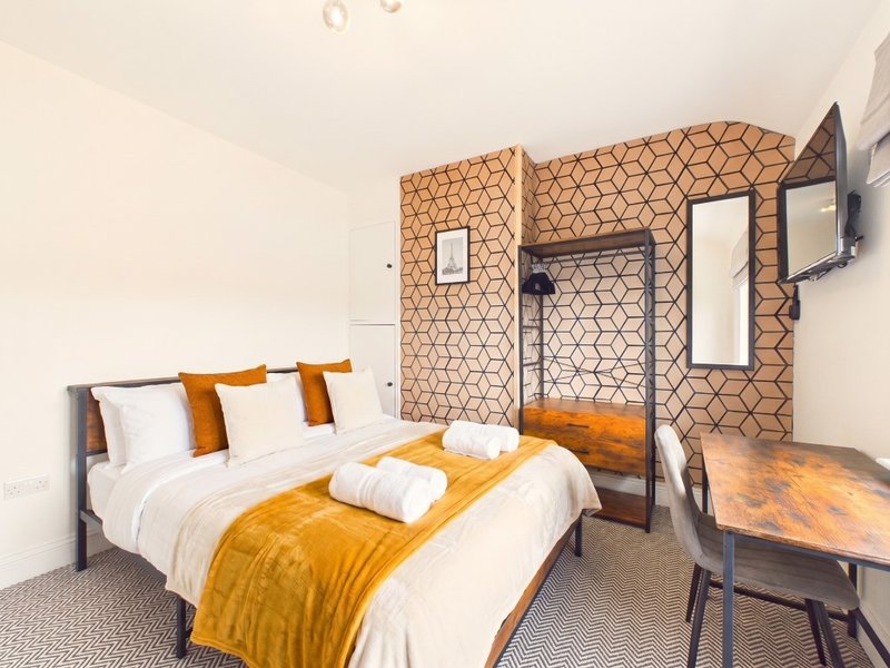 Modern bedroom with double bed, orange throw, white pillows and geometric patterned wall feature