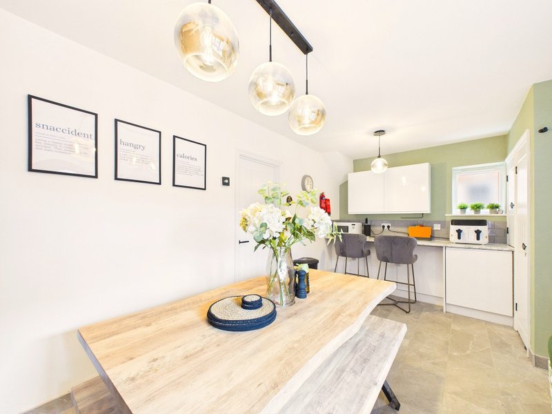 Modern kitchen-diner with wooden table, pendant lights, white cabinetry and green accent wall