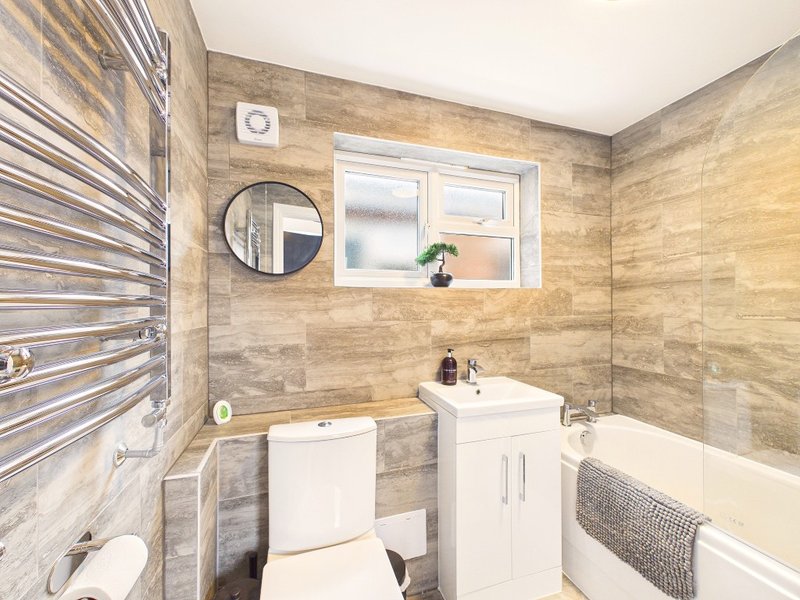 Modern bathroom with white vanity, toilet, bathtub, radiator and round mirror