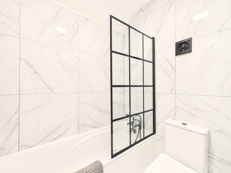 Modern bathroom with marble-effect tiles, black-framed shower enclosure and white toilet