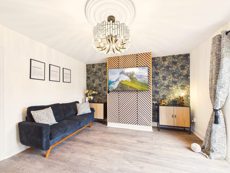 Modern living room with blue velvet sofa, wooden floor, decorative wall panels and ceiling light fixture