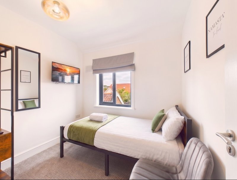 Bright modern bedroom with single bed, green bedding, framed wall art and window view