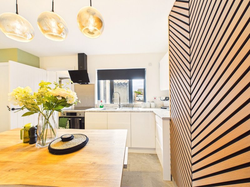 Modern kitchen with wooden dining table, pendant lights, white cabinetry and striped room divider