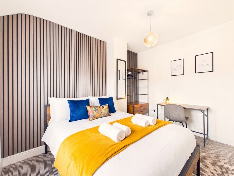 Modern bedroom with two single beds, yellow bedding, blue cushions, wooden headboard wall, and pendant lighting