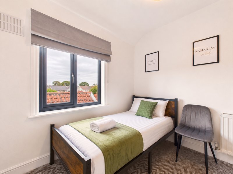 Bedroom with single bed, green bedding, wooden frame, chair, and window overlooking countryside