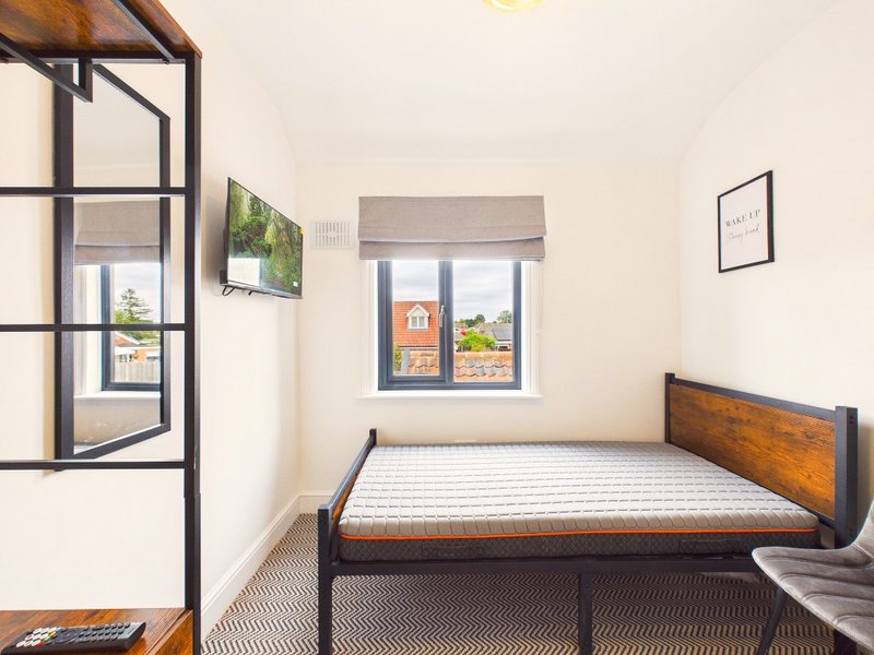 Bedroom with single bed, wooden frame, window with street view, and framed wall art
