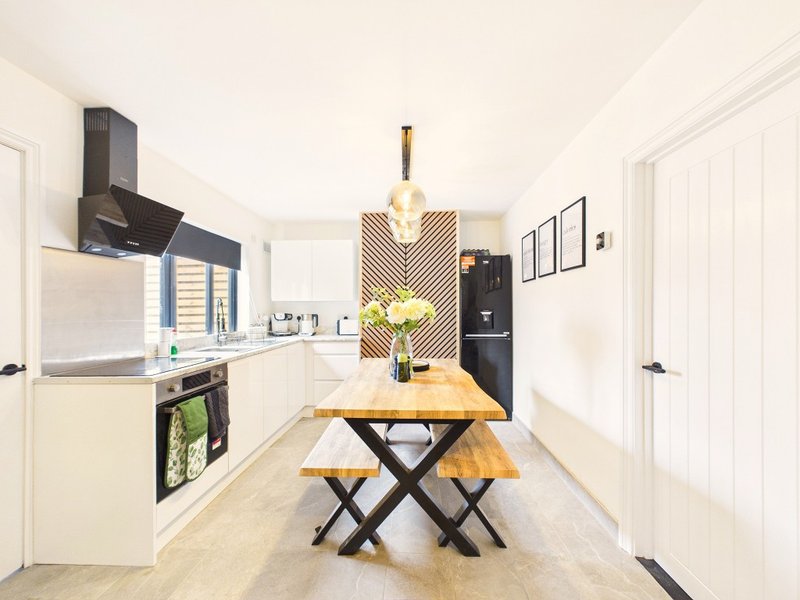 Modern kitchen with white cabinetry, black appliances, wooden dining table and bench seating