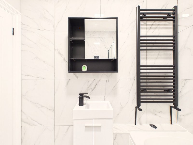 Modern bathroom with marble tiles, white pedestal sink, black mirror cabinet and towel rail