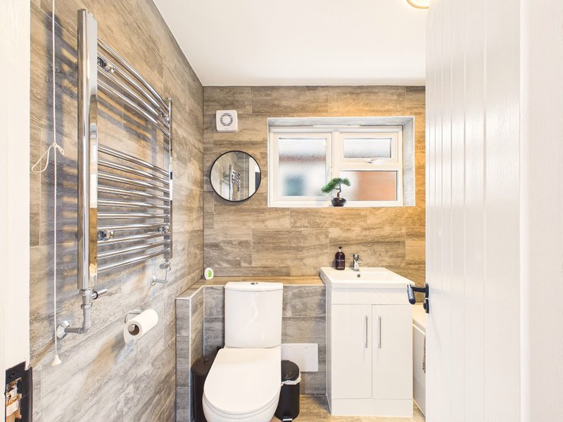 Modern bathroom with heated towel rail, white sink vanity, toilet and circular mirror