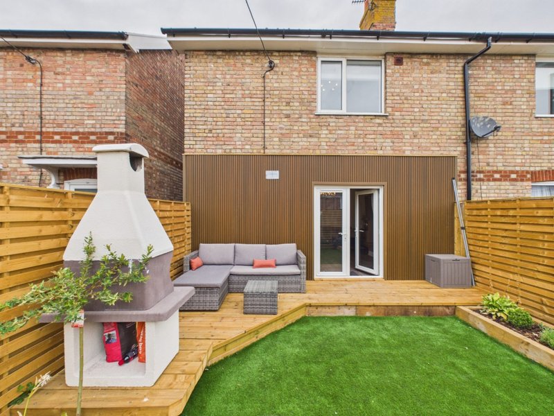 Modern garden with decking, seating area, fireplace and artificial grass surrounded by fencing