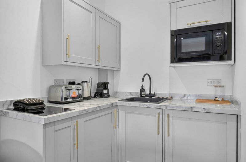 Modern kitchen with white cabinetry, marble countertop, integrated microwave and appliances