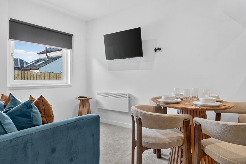 Open-plan living and dining area with blue sofa, wooden table, wall-mounted TV and window view