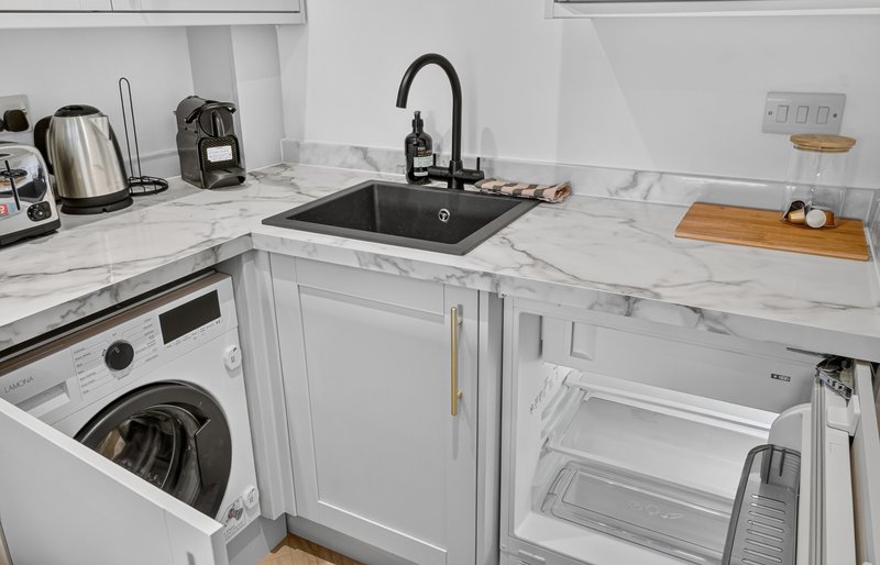 Modern white kitchen with marble countertops, black sink, washing machine and appliances