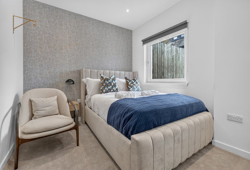 Modern bedroom with cream upholstered bed, blue throw, wooden chair and window