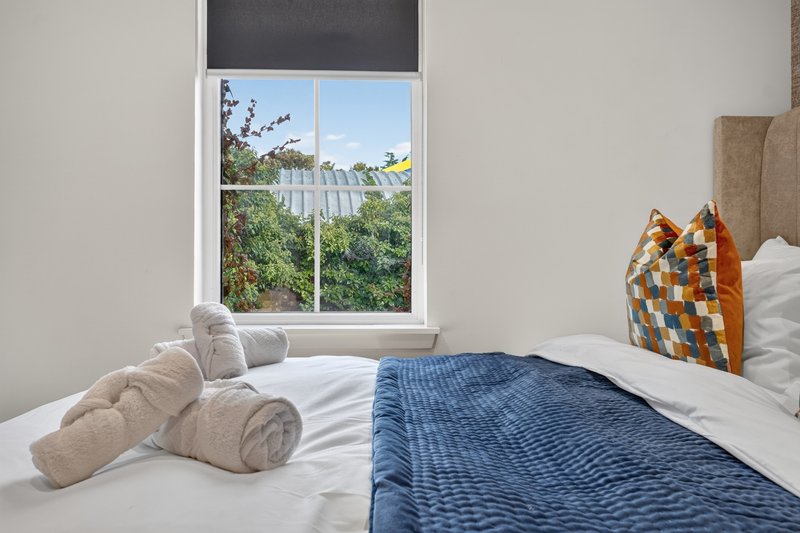 Bright bedroom with double bed, rolled towels, patterned cushion, and window overlooking garden