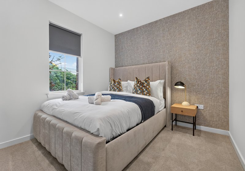 Modern bedroom with upholstered bed, textured accent wall, bedside table and window view