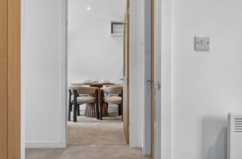 Hallway with white walls leading to dining area with wooden table and chairs