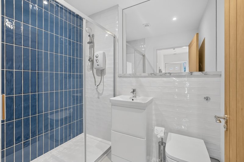Modern bathroom with blue tile shower, white vanity, mirror and toilet
