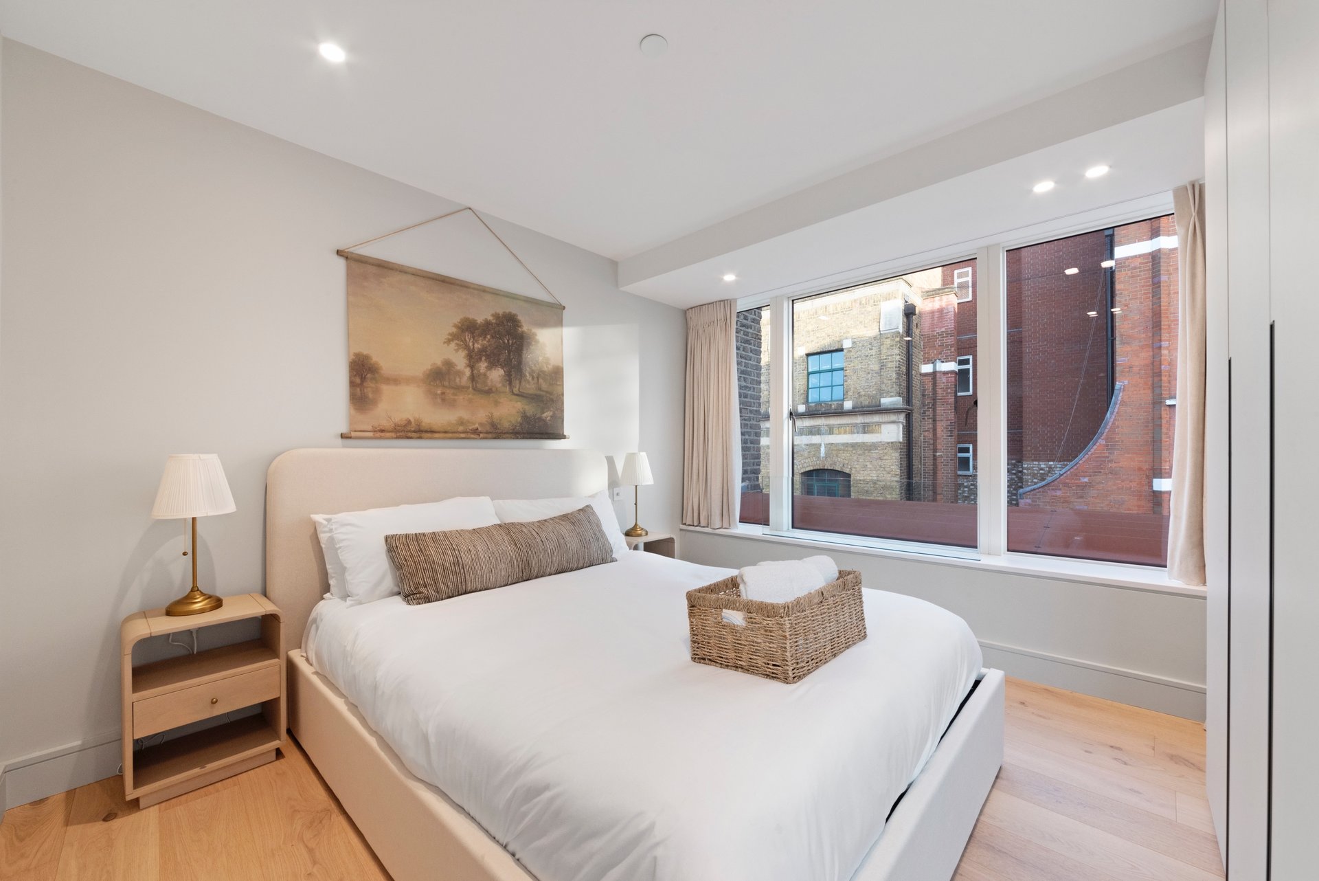Modern bedroom with double bed, wooden bedside table, wall art, and large windows overlooking city