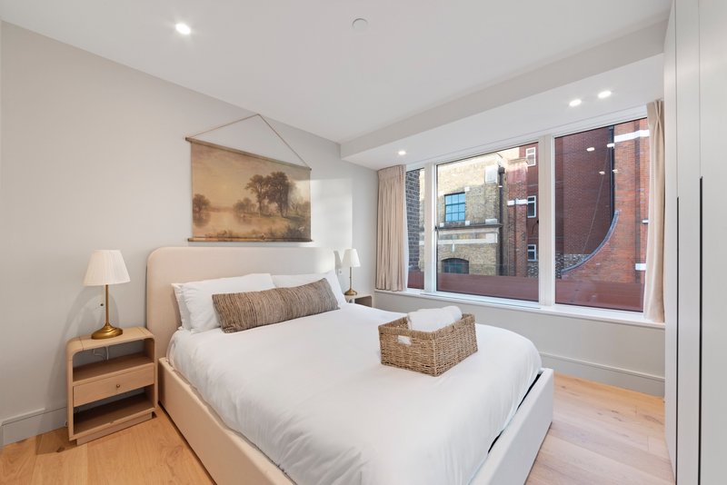 Modern bedroom with double bed, wooden bedside table, wall art, and large windows overlooking city