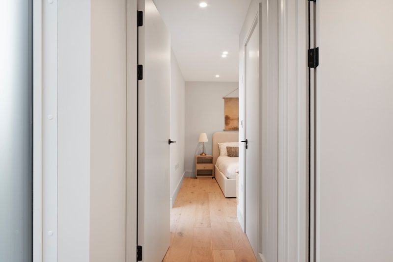 Modern hallway with white walls, wooden flooring, recessed lighting and open doors