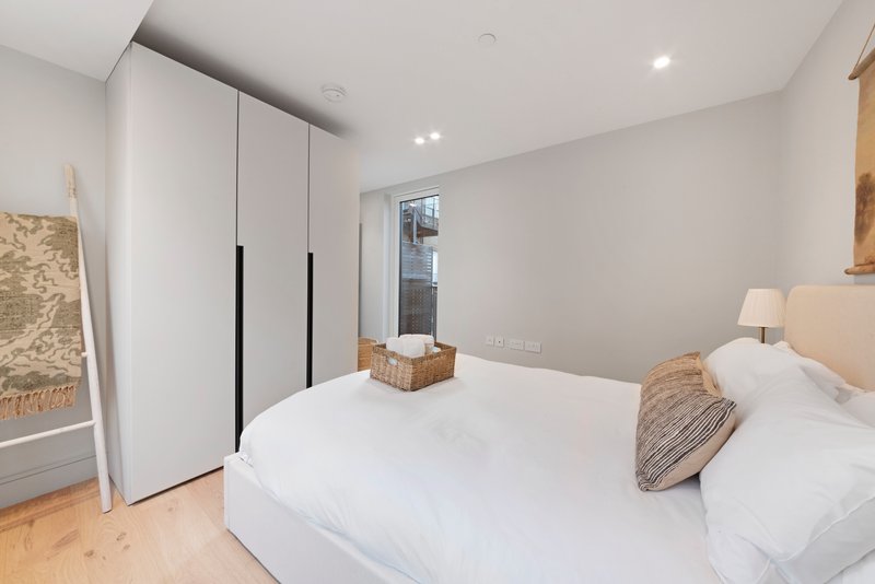 Modern bedroom with double bed, white wardrobe, wooden flooring and bedside lamp