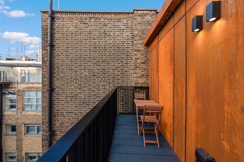 Narrow rooftop terrace with wooden chair, blue decking and brick building views