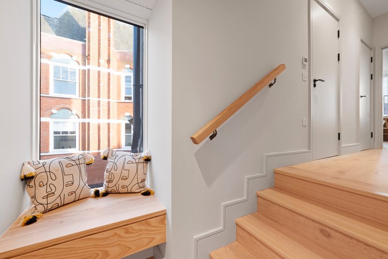 Modern staircase with wooden handrail and steps, window seat with decorative cushions, white walls