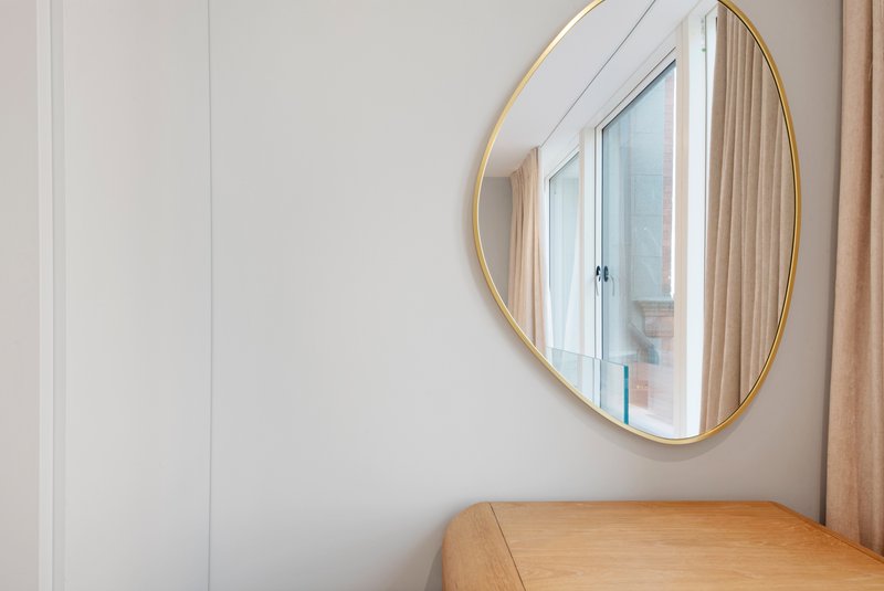 Modern bedroom with wooden bench, circular gold-framed mirror and white wall panelling