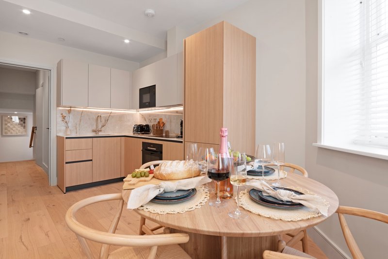 Modern kitchen and dining area with round wooden table, place settings, and contemporary cabinetry