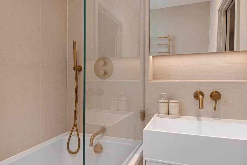 Modern bathroom with white sink, brass fixtures, glass shower enclosure and neutral tile