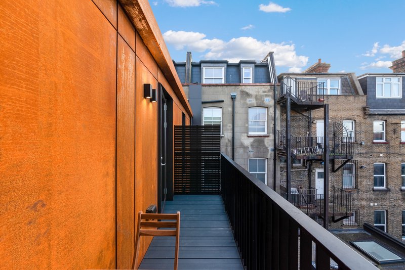 Narrow rooftop terrace with orange wall, wooden chair, and city street view