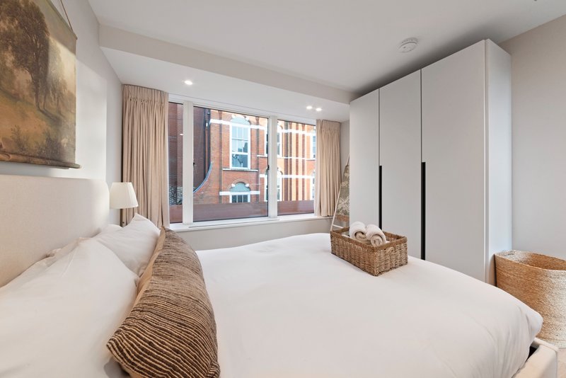 Modern bedroom with two white beds, large window with city views, wardrobe and woven storage baskets