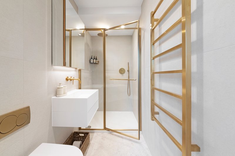 Modern bathroom with white vanity, gold fixtures, glass shower enclosure and heated towel rail