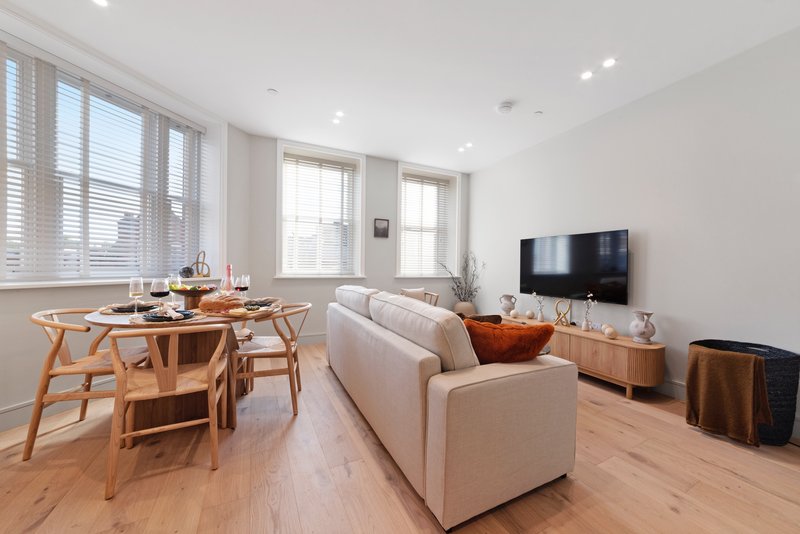 Open-plan living room with dining table, cream sofa, TV, wooden floors and large windows
