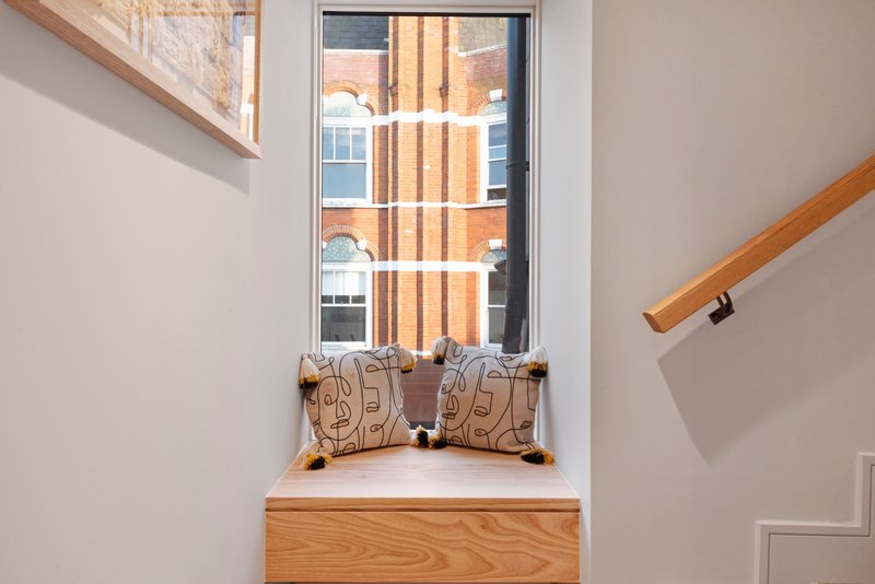 Window seat with wooden storage box, cushions and view of brick building exterior